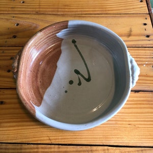 May include: A ceramic bowl with a light gray glaze and a brown rim. The bowl has a green swirl design and a few green dots.