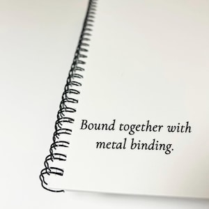 May include: A white notebook with a black metal binding. The notebook is bound together with metal binding.