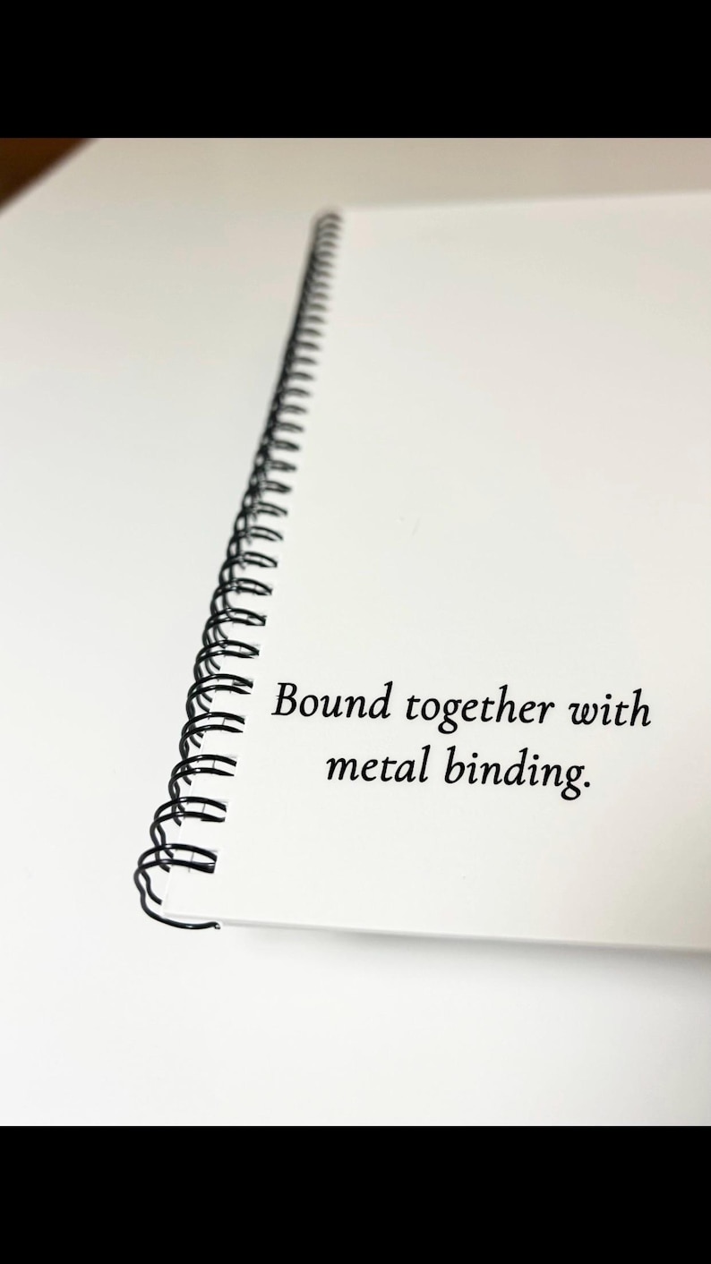 May include: A white notebook with a black metal binding. The notebook is bound together with metal binding.