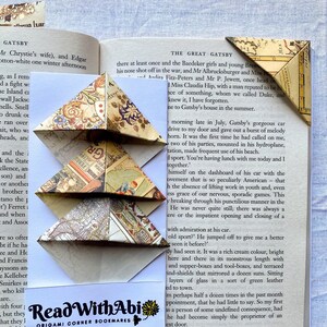 Könnte beinhalten: Drei Origami-Eck-Lesezeichen aus Vintage-Kartenpapier, gestapelt auf einer Buchseite. Die dreieckigen Lesezeichen sind gefaltet. Der Text "Read with Abi" ist sichtbar. Das Buch ist geöffnet.