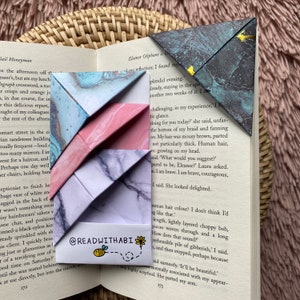 Könnte beinhalten: Dreieckige Lesezeichen aus Papier mit Marmormustern in Blau, Rosa und Grau. Eines hat goldene Details. Der Text "@READWITHABI" ist auf einem zu sehen, mit einer Bienen- und Blumenillustration. Ideal zum Markieren von Seiten in Büchern.