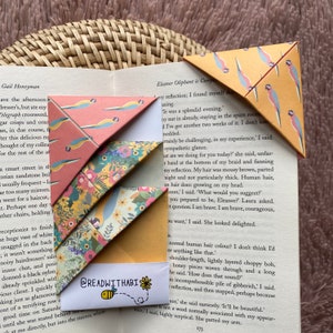 Könnte beinhalten: Eine Auswahl an bunten Papier-Lesezeichen mit verschiedenen Mustern, darunter Papageien und Blumen. Ein Lesezeichen zeigt den Text "@READWITHABI" und eine Bienen-Illustration.