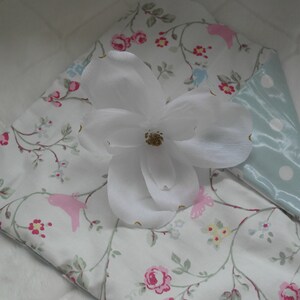 May include: A white pillowcase with a floral pattern featuring pink and blue flowers, green leaves, and pink birds. The pillowcase has a light blue satin back with white polka dots.