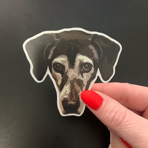 May include: A black and white dog sticker with a sad expression. The sticker is printed on white paper and has a white border.