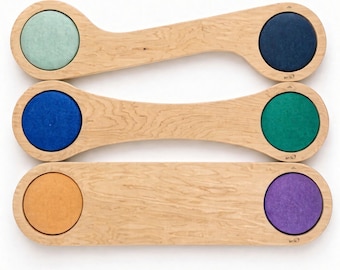 May include: Three light-colored wooden balance boards with curved edges, each featuring two circular cutouts containing felt-like inserts in pastel green, dark blue, bright blue, emerald green, orange, and purple. Text reads: Stepping stones sold separately.