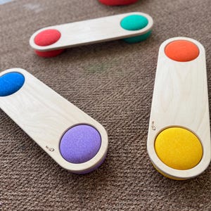 Puede incluir: Cuatro vigas de equilibrio de madera con almohadillas redondas, suaves y coloridas en cada extremo. Las almohadillas son rojas, verdes, moradas y amarillas.