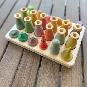 May include: A wooden tray containing an assortment of colourful wooden pegs and small wooden shapes. The pegs are arranged in rows and the shapes are scattered around the tray.