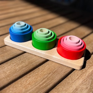 Op de afbeelding: Drie houten stapelringen, elk in een andere kleur: blauw, groen en rood. De ringen zijn gestapeld op een houten basis.