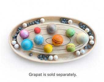 May include: An oval wooden tray with concentric etched rings, containing various colorful wooden spheres, small grey flower-shaped pieces, and white wooden balls. The tray features a natural wood grain finish. Text reads: Grapat is sold separately.