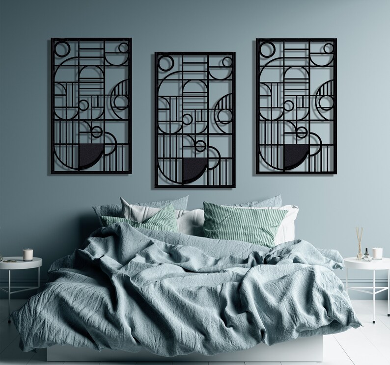 May include: Three black metal wall sculptures with geometric designs, featuring circles and lines, hanging above a bed with blue bedding.