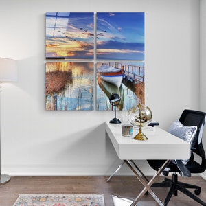 May include: A four-panel canvas print depicting a tranquil lake scene with a small boat moored at a wooden jetty. The sky is a vibrant blue with fluffy clouds and a setting sun. The water is calm and reflective, with reeds and grasses growing along the shore. The print is ideal for adding a touch of nature to any room.