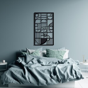 May include: A black metal wall art piece with geometric shapes and lines. The art is hanging on a light blue wall above a bed with a light blue duvet cover and white and green patterned pillows.