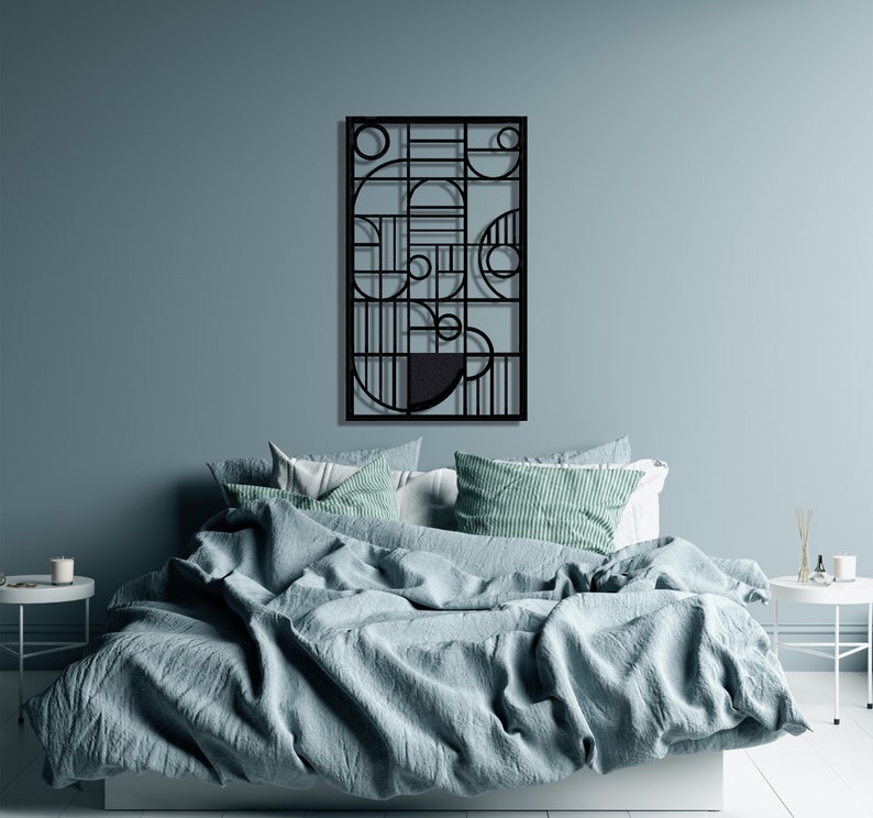 May include: A black metal wall art piece with geometric shapes and lines. The art is hanging on a light blue wall above a bed with a light blue duvet cover and white and green patterned pillows.