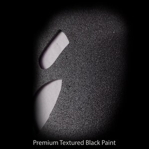 May include: Close-up of a textured black surface with two white shapes cut out. The surface has a fine, grainy texture.  Premium Textured Black Paint.