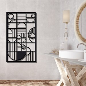 May include: Black metal wall decor with a geometric design featuring circles and lines. The decor is hanging on a white wall in a bathroom setting.