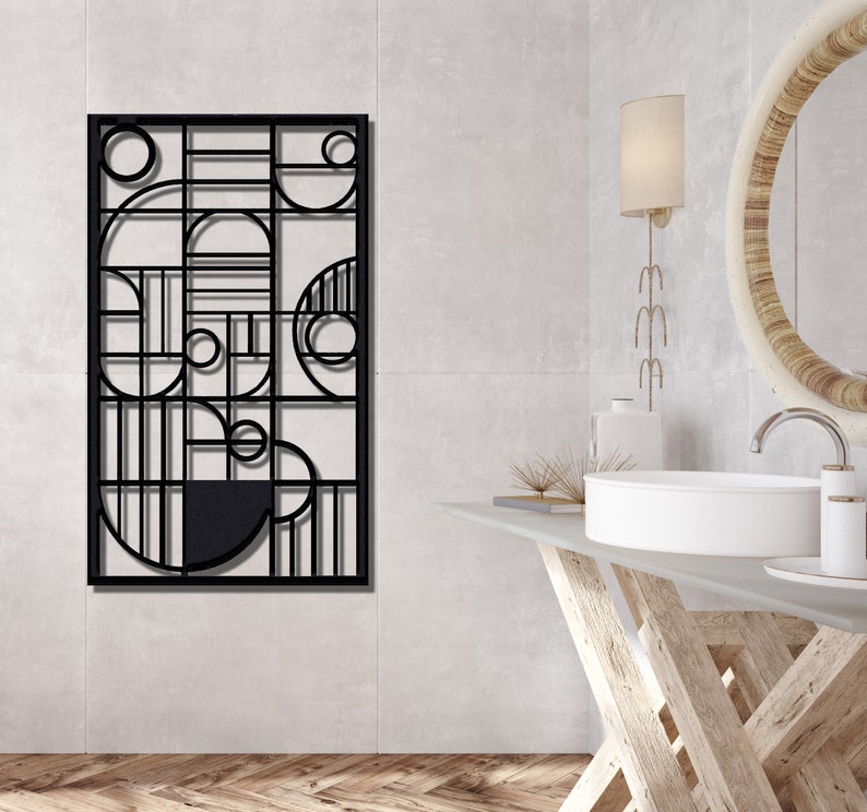 May include: Black metal wall decor with a geometric design featuring circles and lines. The decor is hanging on a white wall in a bathroom setting.