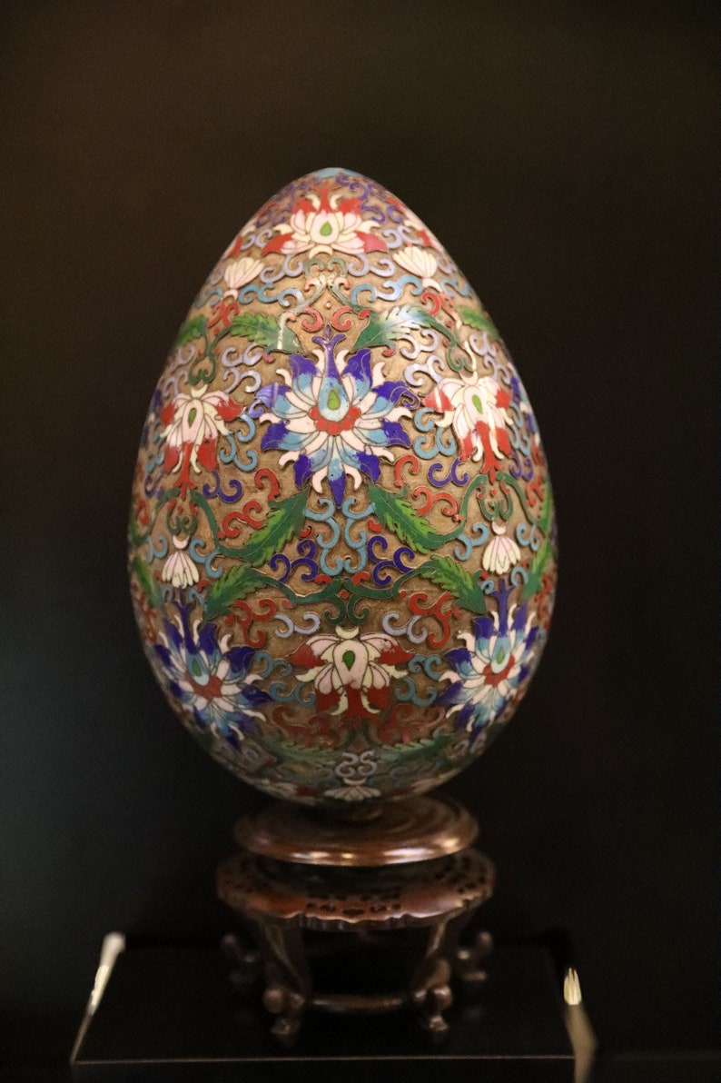 May include: An ornate, egg-shaped decorative object with a floral design in red, white, blue, and green. The egg sits on a small, dark wooden stand. The intricate pattern covers the entire surface.