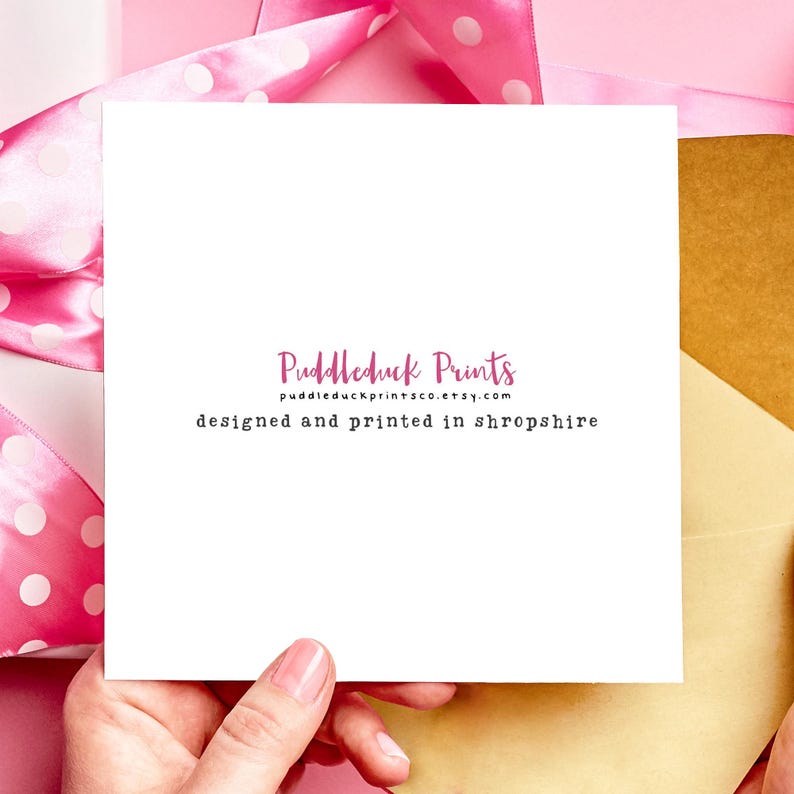 May include: A white card with the text "Puddleduck Prints" and "designed and printed in shropshire" in a pink and black font. The card is held by a hand against a pink background with a pink ribbon.