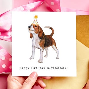May include: A birthday card with a watercolour illustration of a beagle wearing a party hat. The dog is brown, white, and black. The card has the text "happy birthday to yooooooou!" in a black, sans-serif font.