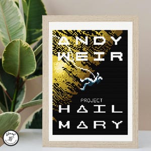 Puede incluir: Un patrón de punto de cruz enmarcado con un diseño pixelado de una figura flotando en el espacio sobre un fondo negro y dorado. El texto dice ANDY WEIR PROJECT HAIL MARY en una fuente blanca de bloques. El marco tiene un acabado de madera clara.