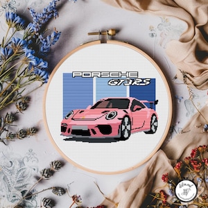 Può includere: Un telaio da ricamo a punto croce con un design di auto Porsche GT3RS rosa. Il testo "PORSCHE GT3RS" è sopra l'auto, su uno sfondo blu. Il ricamo è inserito in un telaio di legno.