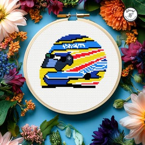 Può includere: Ricamo a punto croce di un casco da corsa in un telaio di legno. Il design del casco presenta colori blu, giallo, rosso e bianco. Lo sfondo è bianco e il telaio è circondato da fiori colorati.