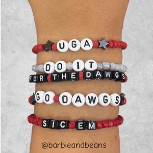 May include: Four beaded bracelets with the words "UGA", "DO IT FOR THE DAWGS", "GO DAWGS", and "SIC EM". The bracelets are red, white, and black.