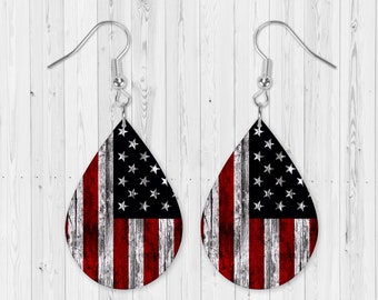May include: A pair of teardrop-shaped earrings featuring a distressed American flag design. The earrings are red, white, and blue with a woodgrain texture.