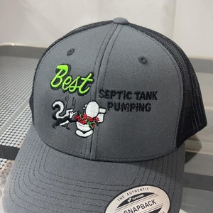 May include: A gray and black trucker hat with a white embroidered design of a cartoon skunk holding a toilet plunger. The text "Best Septic Tank Pumping" is embroidered in black on the hat. The hat has a black mesh back and a white "Snapback" label.