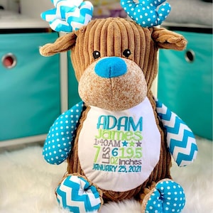 May include: A brown corduroy reindeer plush toy with blue and white polka dot and chevron patterned accents. The toy is personalized with the name "Adam James", birth date "January 25, 2021", time "1:40 AM", weight "7 lbs 6 oz", and length "19.5 inches".