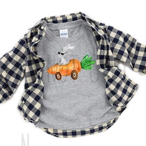 Puede incluir: Una camiseta gris de manga larga con un gráfico de un conejito blanco con gafas de sol conduciendo un coche zanahoria. La camiseta está debajo de una camisa abotonada a cuadros azul y crema.
