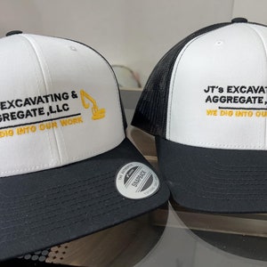 May include: Two white and black trucker hats with a yellow embroidered logo that says "JT's Excavating & Aggregate, LLC" and "We Dig Into Our Work".