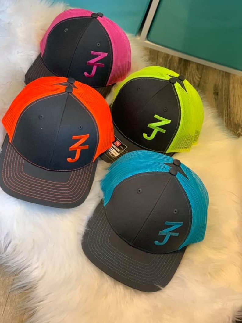 May include: Four black trucker hats with different colored mesh panels. The hats have a white embroidered "ZJ" logo on the front. The mesh panels are pink, green, orange, and blue.