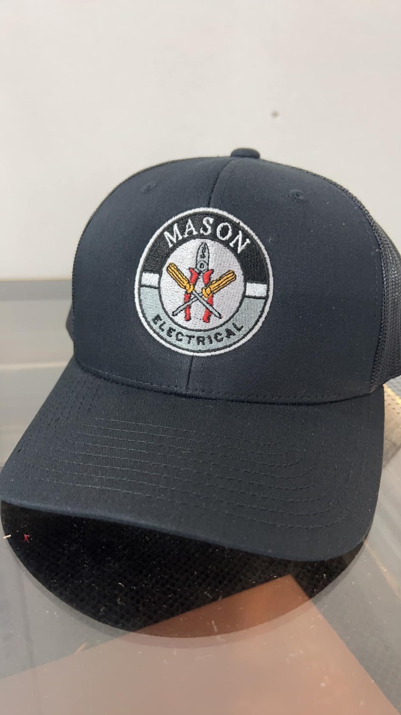 May include: Black trucker hat with a black and white embroidered logo that says "MASON ELECTRICAL" with a pair of crossed screwdrivers in the center.