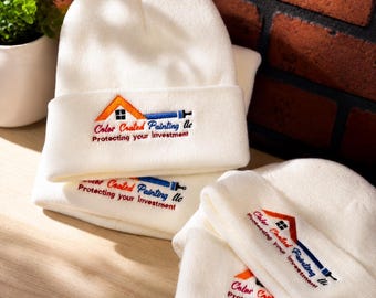 Puede incluir: Una pila de gorros de punto blancos con un logotipo bordado que muestra un tejado naranja, un pincel azul y el texto rojo Color Coated Painting Llc, seguido del texto negro Protecting your investment en el borde doblado.