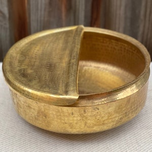 May include: A gold-toned brass bowl with a hinged lid. The bowl has a hammered texture and a rounded shape.