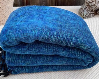 Peut inclure: Une couverture en laine bleue pliée avec un motif subtil. La couverture est douce et chaude, idéale pour se blottir sur le canapé.