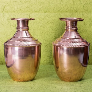 May include: Two copper vases with a shiny finish and a beaded design around the middle. The vases are on a green textured background.