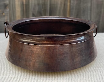 Könnte beinhalten: Ein großer, gehämmerter Kupfertopf mit zwei Griffen. Der Topf hat eine dunkelbraune Patina und ist oval.