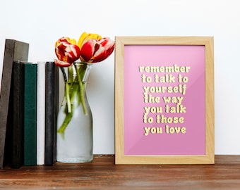 May include: A framed pink print with the text "remember to talk to yourself the way you talk to those you love" in yellow letters. The print is sitting on a wooden surface with a vase of red and yellow tulips.