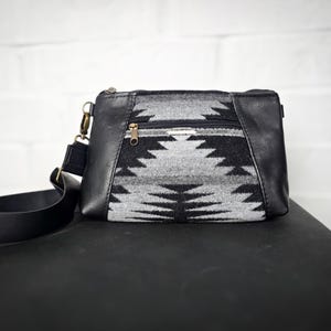 Puede incluir: Un bolso bandolera de patrón blanco y negro con una correa de cuero negro y cierre de cremallera.