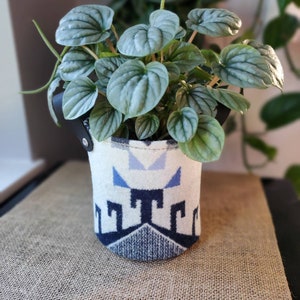 Könnte beinhalten: Eine kleine Pflanze mit silbernen Blättern in einem Stofftopf mit weißem und blauem Muster und einem schwarzen Ledergriff.