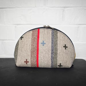 May include: A half-round beige zippered pouch with a red stripe and a pattern of blue and black crosses.