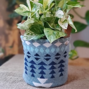 Könnte beinhalten: Eine weiß-grüne panaschierte Pflanze in einem blauen und weißen gemusterten Stoff-Hängepflanztopf mit braunen Lederriemen.