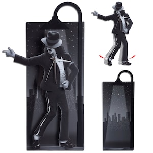 May include: A black and white wall clock featuring a silhouette of a person dancing. The clock is shaped like a street lamp with a spotlight shining on the person. The background is a cityscape at night.