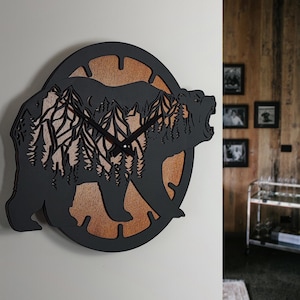 May include: A black bear-shaped wall clock with a mountain and forest design. The clock features a wooden background and black hands. The bear's silhouette is cut out, revealing the mountain and forest scene.