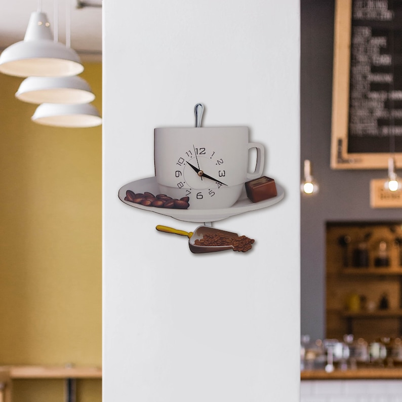 May include: White coffee cup clock with black hands and numbers. The cup is on a white saucer with coffee beans. A small scoop of coffee beans is below the saucer.