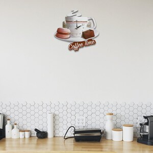 May include: White ceramic coffee cup clock with a steaming cup of coffee, a pink macaron, and a chocolate bar on a white plate. The clock face has black hands and black numbers. The clock reads "Coffee Time".
