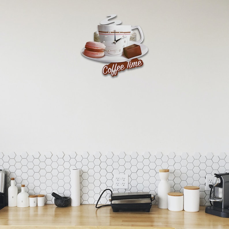 May include: White ceramic coffee cup clock with a steaming cup of coffee, a pink macaron, and a chocolate bar on a white plate. The clock face has black hands and black numbers. The clock reads "Coffee Time".