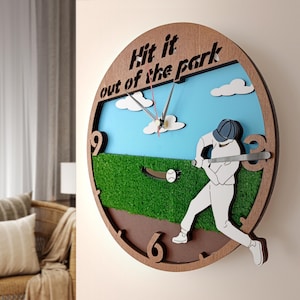 Puede incluir: Un reloj de pared de madera con temática de béisbol. La esfera del reloj presenta a un jugador de béisbol bateando una pelota, una pelota de béisbol y el texto "Hit it out of the park". El fondo incluye un cielo azul con nubes y hierba verde.